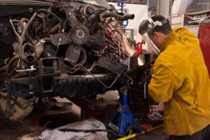 An Auto Body Repair student grinds the frame of a car.