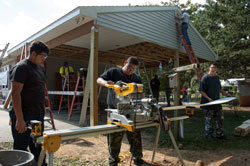 Students cut vinyl siding with a chop saw on the site of a house renovation project.