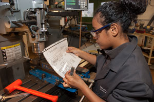 A machining student checks the blueprint of a part to be made on the milling machine.