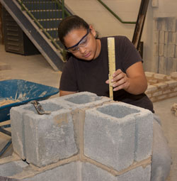 A Bricklaying student checks the height of a wall while laying block.
