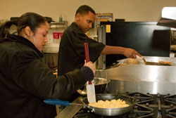 Two students cook breakfast at the stove.