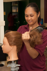 A Cosmetology student combs a mannequin's hair.