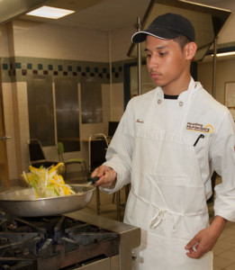 A Culinary Arts student tosses food in a frying pan.