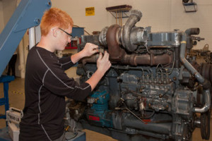 A student uses a wrench to adjust a large diesel engine.