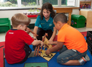 An Early Childhood Education student supervises children playing with toy dinosaurs.