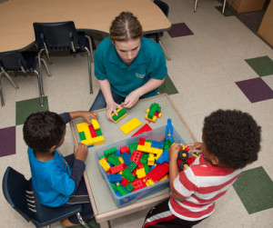 An Early Childhood Education student works with two preschool children at a table. 