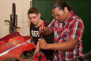Two students work on repairing a motorcycle.