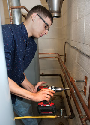 A Plumbing and Heating student attaches copper tubing to a wall.