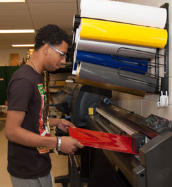 A student learns how to print on vinyl material in the Printing and Graphic Communications lab.