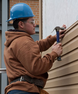 Carpentry student installs vinyl siding on the exterior of a building.