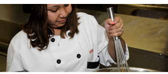 A Culinary Arts student uses a whisk to blend ingredients in a bowl.