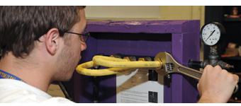 A Plumbing and Heating student uses a wrench to tighten a hose connection.