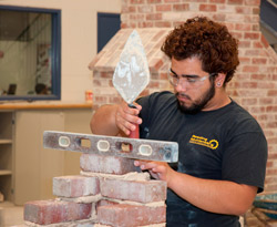 A Bricklaying student checks the level while tapping a brick with a trowel.