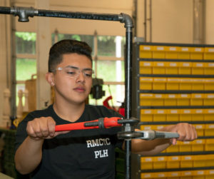 A student in the Plumbing & Heating program uses wrenches to tighten a pipe fitting.