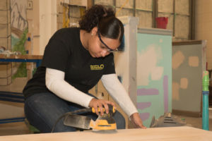 A Painting & Decorating student uses a power sander on a table top.